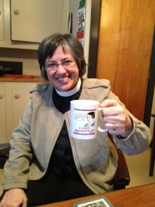 The Rev. Anne Emry drinking coffee in Tim's office out of her 2013 mug.